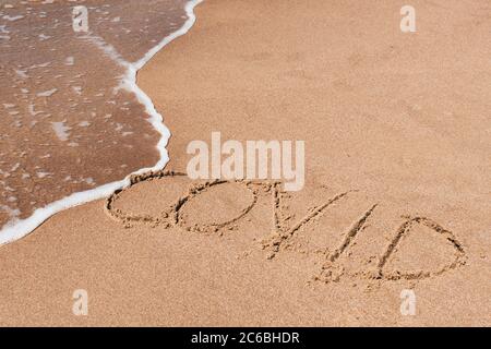 Covid libero, fermata Covid, spiaggia sicura e vacanza, parola scritta sulla sabbia con lavaggio a onde e pulizia Foto Stock