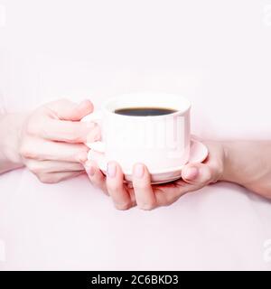 Mani femminili che tengono una tazza rosa di caffè nero su sfondo rosa. Spazio di copia Foto Stock