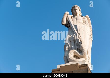 Antica statua dell'Arcangelo San Michele che combatte il drago con sfondo blu e spazio per il testo Foto Stock