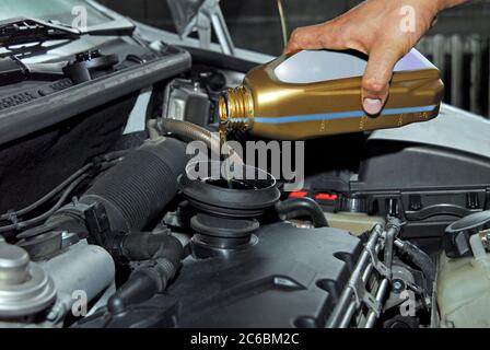 Aggiunta di olio ad un'automobile, la mano dell'uomo che tiene una ciotola di olio motore e versato nel motore Foto Stock