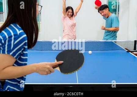 Divertimento di coppia giocando a ping pong o Ping pong al coperto insieme tempo libero con la competizione in giochi sportivi in casa. Padre madre e figlia famiglia asiatica Foto Stock