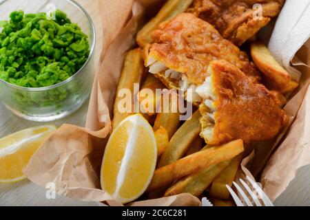 Pesce e patatine fatte in casa con limone e piselli verdi Foto Stock