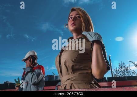 Primo piano di un elegante modello glamour in elegante abito presso la base di costruzione vicino a Workker Builder. Foto Stock
