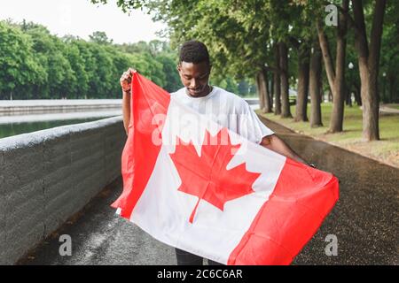 Bell'uomo afro-americano con bandiera canadese, in piedi all'aperto. Foto Stock