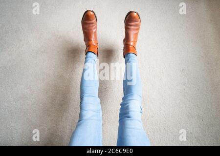 Persona con gambe allungate che indossa stivali marroni e jeans blu. Piedi fuori terra, stile, alla moda, moda, divertimento Foto Stock