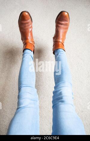 Persona con gambe allungate che indossa stivali marroni e jeans blu. Piedi fuori terra, stile, alla moda, moda, divertimento Foto Stock