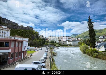 Lourdes, Francia - 18 giugno 2018: Strada e l'alto abete rosso sulla riva di un fiume di montagna veloce Gave de Pau Foto Stock