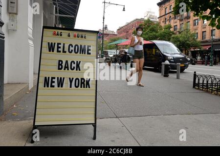 New York City, Stati Uniti. 8 luglio 2020. Una donna che indossa una maschera al tempo di COVID-19 cammina lungo Columbus Ave. Dove un cartello si trova fuori Rag e negozio di moda ossa che accoglie i newyorkesi di nuovo a fare shopping mentre New York City si sposta nella fase 3 della riapertura, a New York, NY, 8 luglio 2020. (Anthony Behar/Sipa USA) Credit: Sipa USA/Alamy Live News Foto Stock