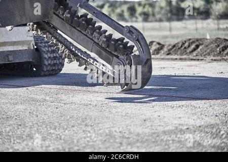 Primo piano di una catena di scavatrici in movimento che scavano una trincea nello sporco con gli operatori che si muovono lateralmente Foto Stock