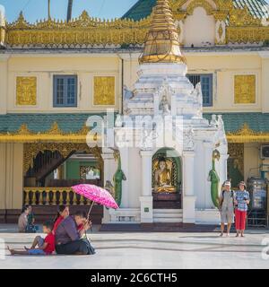 Una giovane famiglia che prega in un santuario del Buddha alla Pagoda Shwedagon a Yangon, Myanmar Foto Stock
