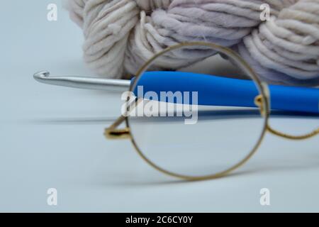 Paio di occhiali da lettura granny in uno studio di sfondo bianco primo piano con palla di lana di farinata d'avena organica e un gancio a crochet in metallo e plastica Foto Stock