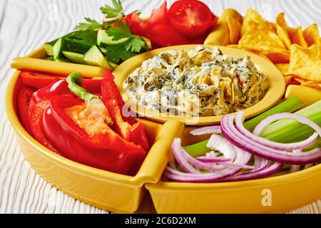 Set per immersione con carciofi di spinaci con patatine di tortilla, cetriolo, bastoncini di sedano, fette di pomodoro e peperone rosso, vista panoramica dall'alto, primo piano Foto Stock