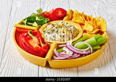 Set per immersione con formaggio di carciofi spinaci con patatine di tortilla, cetriolo, bastoncini di sedano, fette di pomodoro e peperone rosso, vista panoramica dall'alto, primo piano Foto Stock