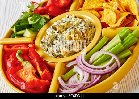 Set per immersione con formaggio di carciofi spinaci con patatine di tortilla, cetriolo, bastoncini di sedano, fette di pomodoro e peperone rosso, vista panoramica dall'alto, primo piano Foto Stock