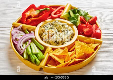 Set per immersione con formaggio di carciofi spinaci con patatine di tortilla, cetriolo, bastoncini di sedano, fette di pomodoro e peperone rosso, vista orizzontale dall'alto, primo piano Foto Stock