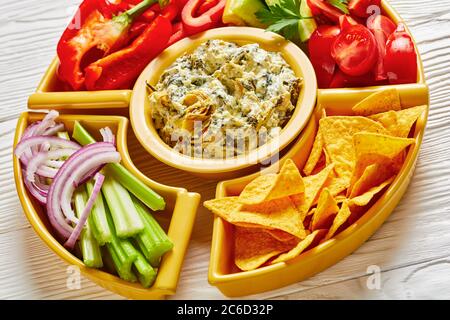 Primo piano di un tuffo al formaggio Spinach Artichoke con patatine di tortilla, cetriolo, bastoncini di sedano, fette di pomodoro e peperone rosso, vista orizzontale da abò Foto Stock