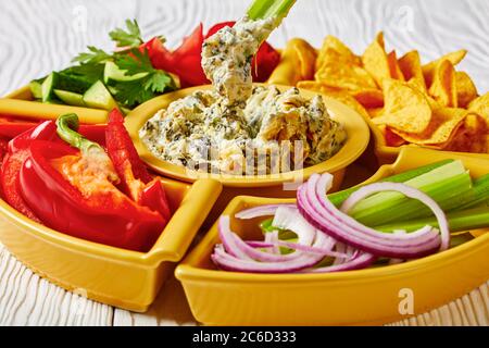 Primo piano di un tuffo al formaggio Spinach Artichoke con patatine di tortilla, cetriolo, bastoncini di sedano, fette di pomodoro e peperone rosso, vista orizzontale da abò Foto Stock