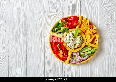 Primo piano di salsa al formaggio Spinach con foglie di carciofi, patatine di tortilla, cetriolo, bastoncini di sedano, fette di pomodoro e peperone rosso, vista orizzontale Foto Stock