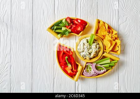 Primo piano di salsa al formaggio Spinach con foglie di carciofi, patatine di tortilla, cetriolo, bastoncini di sedano, fette di pomodoro e peperone rosso, vista orizzontale Foto Stock