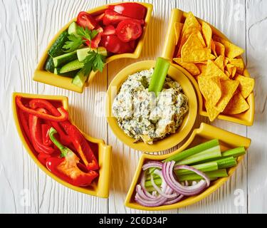 Primo piano di salsa al formaggio Spinach con foglie di carciofi, patatine di tortilla, cetriolo, bastoncini di sedano, fette di pomodoro e peperone rosso, vista orizzontale Foto Stock