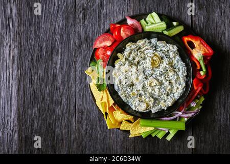 Spinach carciofo formaggio a foglia di carciofo immergere in una ciotola con tortilla chips, cetriolo, bastoncini di sedano, fette di pomodoro e peperone rosso, vista orizzontale da abò Foto Stock