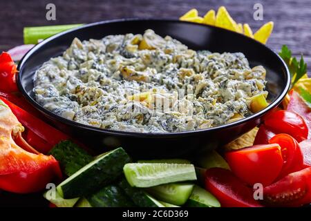 Primo piano di Spinach carciofo formaggio a foglia di carciofo immergere in una ciotola con tortilla chips, cetriolo, bastoncini di sedano, fette di pomodoro e peperone rosso, paesaggio vi Foto Stock