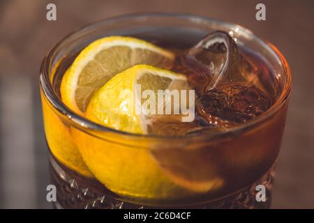 Bicchiere di tè freddo di Long Island con fetta di limone e paglia. Primo piano di una bevanda alcolica color ambra con ghiaccio sul tavolo in un bar, caffetteria Foto Stock