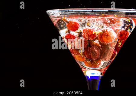 Bicchiere di rinfrescante drink estivo con frutti di bosco e cubetti di ghiaccio sul tavolo vicino.rinfrescante bevanda estiva con uva spina. Foto Stock