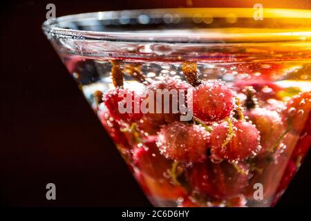 Bicchiere di rinfrescante drink estivo con frutti di bosco e cubetti di ghiaccio sul tavolo vicino.rinfrescante bevanda estiva con uva spina. Foto Stock