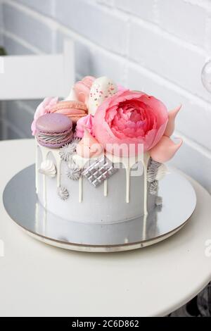 Torta grigia moderna con fiori di pony rosa, cioccolato e macaroon per un matrimonio o una celebrazione. Sfondo bianco. Foto Stock