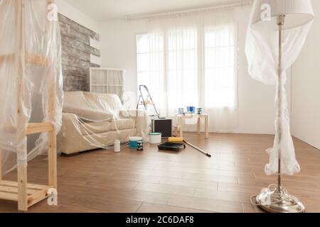 Appartamento con nessuno in esso pronto per un lavoro di ristrutturazione. Foglio di plastica. Casa durante la ristrutturazione, decorazione e pittura. Manutenzione degli appartamenti interni. Rullo, scala per riparazione casa Foto Stock
