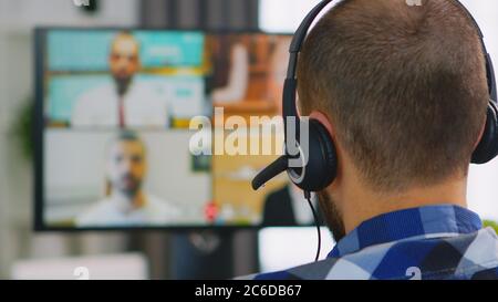 Giovane imprenditore in sedia a rotelle che accende le cuffie durante una videochiamata aziendale. Foto Stock