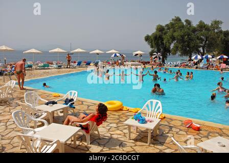 I vacanzieri, principalmente donne, si divertono in una lezione di ginnastica in piscina presso un hotel, Corfù, Grecia, e altri seduti intorno a rilassarsi al sole Foto Stock