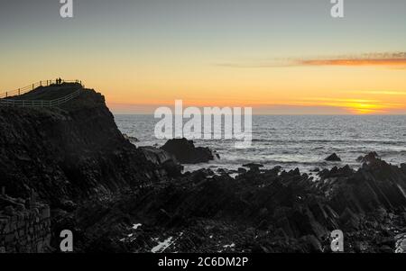 Coppia che guarda il tramonto da Hartland Quay - Hartland, Devon, UK Foto Stock