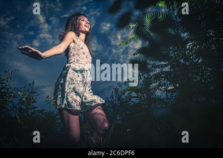 Jolly ragazza che danzano all'aperto in estate in erba alta. È vestita in abito estivo e catched danzare liberamente. Foto Stock