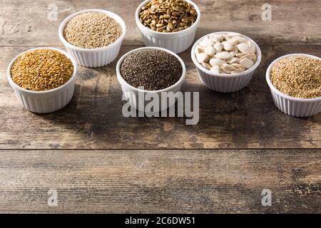 Assortimento di semi diversi in ciotola su tavolo di legno. Zucca, lino, cia, girasole e semi di sesamo. Foto Stock