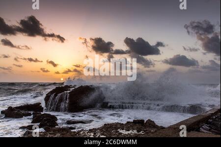 L'antico porto di Cesarea, Israele al tramonto. Le onde si stanno rompendo sulla frangiflutti Foto Stock