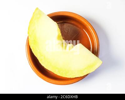 Una fetta di melone fresco di galia in un piccolo piatto marrone isolato su sfondo bianco Foto Stock