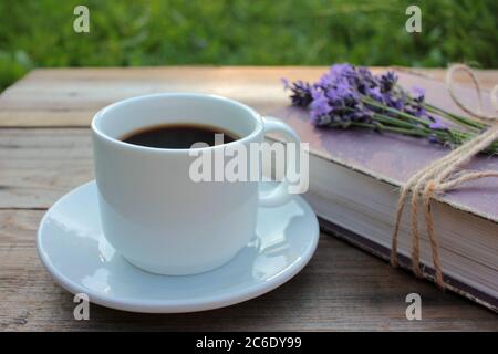 Tazza di caffè e libro antico decorato con fiori di lavanda e legato con spago di iuta su tavolo di legno. Spazio di copia. Messa a fuoco selettiva. Godendo la vita estiva Foto Stock