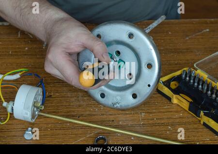 Riparazione di un riscaldatore dell'acqua parte 3/7. Con le mani dell'uomo serrare la vite sulla flangia della caldaia con un cacciavite. Assistenza e riparazione di applicazioni domestiche Foto Stock