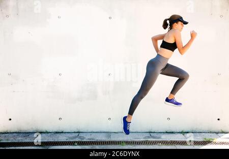 Giovane donna che corre e salta con un muro bianco sullo sfondo Foto Stock