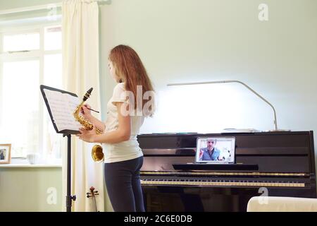 Ragazza che prende online sassofono lezione a casa Foto Stock