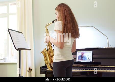 Ragazza che prende online sassofono lezione a casa Foto Stock