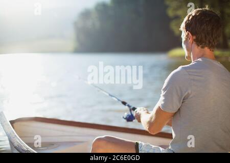 Uomo pesca in barca a remi sul lago calmo Foto Stock