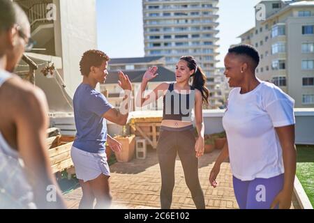 Giovani amici che si allenano e si fanno fare alta sul tetto urbano soleggiato Foto Stock