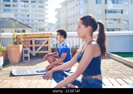 Giovane uomo e donna che pratica yoga sul soleggiato tetto urbano Foto Stock