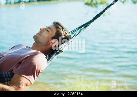 Uomo sereno che si posa in amaca sul lago Foto Stock