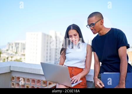 Giovani uomini d'affari con computer portatile che lavorano sul tetto urbano Foto Stock