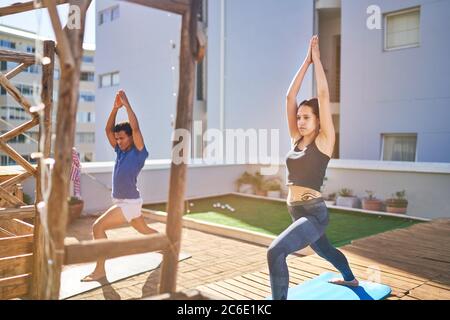 Giovani amici che praticano yoga sul soleggiato tetto urbano Foto Stock