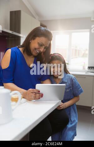 Madre e figlia con tavoletta digitale in cucina Foto Stock